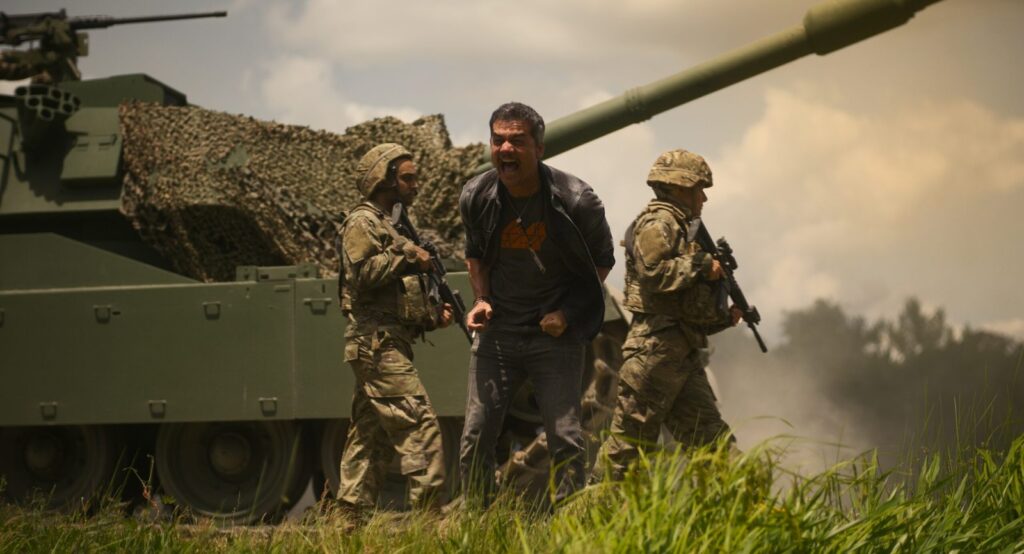 Cena de 'Guerra Civil' co mWagner Moura atrás de um tanque de guerra com soldados